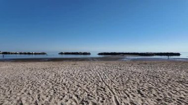 A quiet, sandy beach in Cesenatico, Italy, on a sunny autumn day. The calm Adriatic Sea and rocky breakwaters create a peaceful, off-season scene. High quality 4k footage