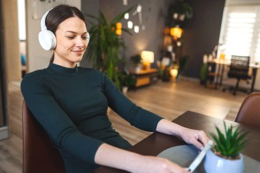 Beyaz kulaklıklı çok mutlu bir genç kız kapalı alanda cep telefonu kullanmaktan zevk alıyor..