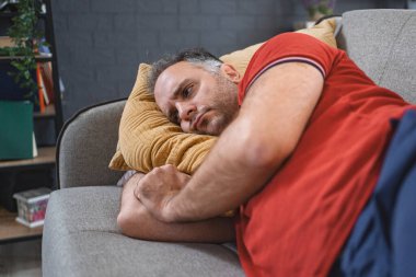 Evde yalnız bir adam kanepeye uzanmış üzgün ve perişan görünüyor..