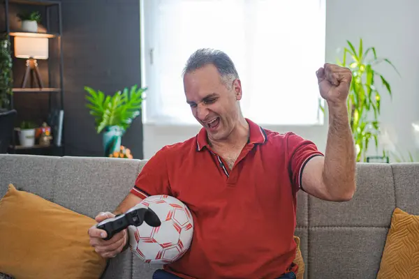 Excited middle aged man playing soccer video game at home..