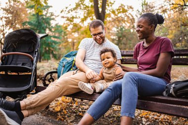 Karışık ırk çiftleri parktaki bir bankta oğullarıyla oturuyor..