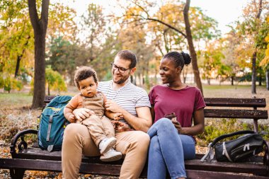 Karışık ırk çiftleri parktaki bir bankta oğullarıyla oturuyor..