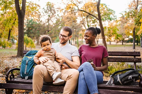 Karışık ırk çiftleri parktaki bir bankta oğullarıyla oturuyor..