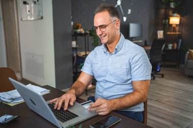 Orta yaşlı, beyaz bir adam internette bilgisayardan alışveriş yapıyor..