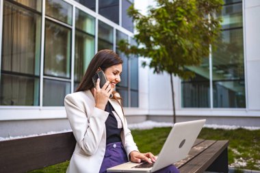 İş kadını dışarıda dizüstü bilgisayarla uğraşırken telefonda konuşuyor..