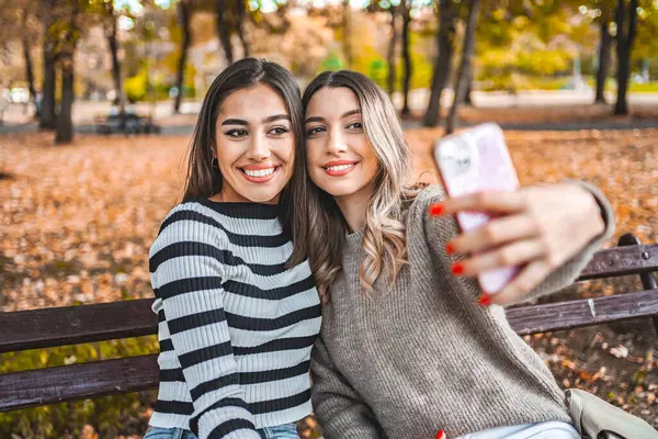 Bir arada duran iki kadın, fotoğraf çekmek için cep telefonu tutuyorlar. Gülümsüyorlar ve poz veriyorlar..