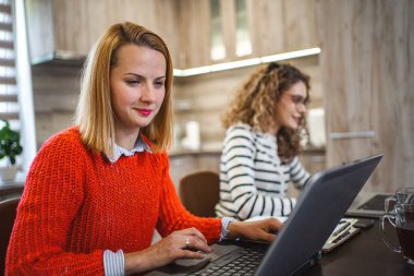 İki kadın bir masada oturuyor, ikisi de bir dizüstü bilgisayara odaklanıyor. Sohbete dalmış ya da bilgisayarla işbirliği içinde çalışıyor gibi görünüyorlar..