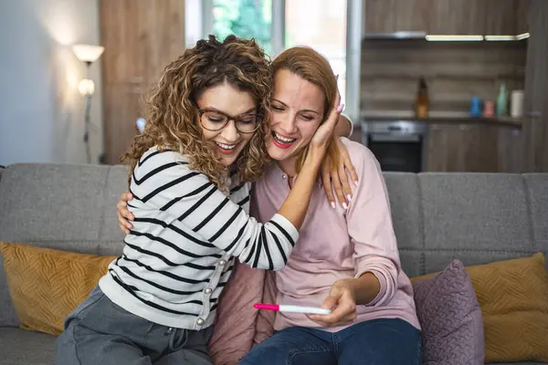 两个女性朋友正坐在客厅的沙发上 在得到怀孕测试结果后 她们都兴奋地拥抱在一起 — 图库照片