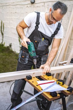 Olgun erkek marangoz, tahtadan bir tahta üzerinde elektrikli tornavida kullanıyor..
