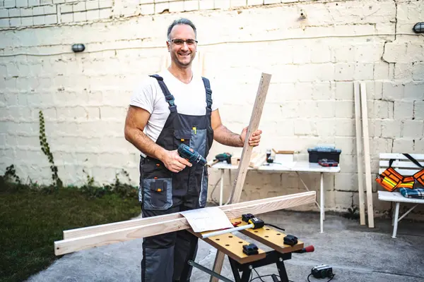 Dojrzały Stolarz Pracujący Elektrycznym Śrubokrętem Drewnianej Desce Zewnątrz — Zdjęcie stockowe