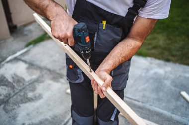 Tahta bir tahta üzerinde elektrikli tornavida kullanan tanınmayan bir erkek marangoz..