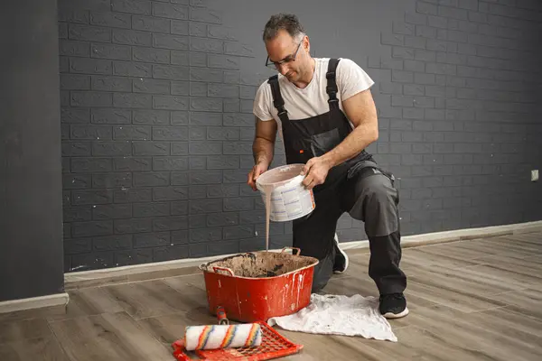 Kneeling Man Pours Paint Large Plastic Container Wears Work Clothes — Stock Photo, Image