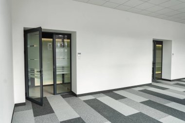 Ofiste sadece iki kapı ve siyah-beyaz kareli zemin bulunan mobilya ve dekorasyondan yoksun bir ofis alanı. Kapılar kapalı, bilinmeyen yerlere açılıyor, zemin ise bir geometrik ekliyor.
