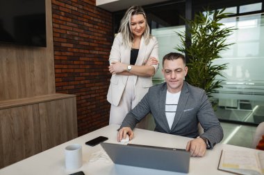 Masada oturan bir adam dizüstü bilgisayardaki işine odaklanmış. Oda iyi aydınlatılmış ve adam ekrana dikkatle bakıyor, daktilo ediyor ve tıklıyor..