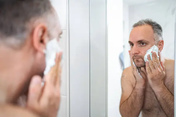 一个男人在浴室里把剃须泡沫涂在脸上 — 图库照片