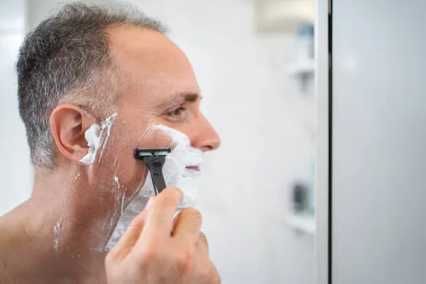 Close up portrait of man in front of shaving mirror in bathroom.