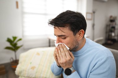 Bir adam peçeteyi burnuna dayayıp üflerken görülüyor. Halka açık bir yerde gibi görünüyor, muhtemelen soğuk algınlığı ya da alerjiyle uğraşıyor..