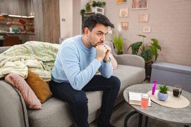 Kahverengi saçlı depresif adam oturma odasındaki kanepede oturuyor. Düşünceli ve endişeli..