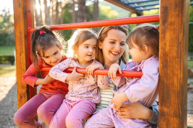 Gülümseyen ve mutlu anne, anaokulu kızı ve ikizleriyle oyun bahçesinde..