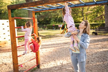 Gülümseyen anne, sevimli kızının oyun parkına çıkmasına yardım ediyor..