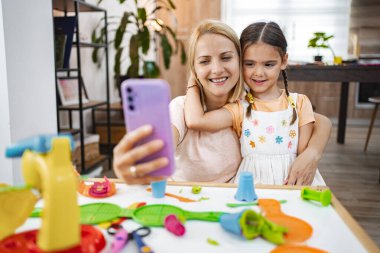 Gülümseyen bir anne ve kızı, masada canlı oyuncaklarla çevrili bir selfie çekerek birlikte eğlenceli bir anın tadını çıkarırlar..