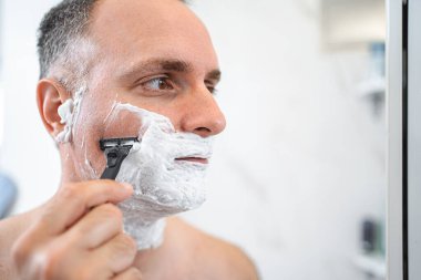 Banyoda tıraş aynasının önünde duran adamın portresini kapat..