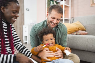 Evde ebeveynler tarafından bakılırken bir çocuk ışıl ışıl gülümser..