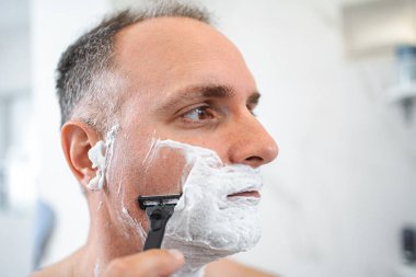 Banyoda tıraş aynasının önünde duran adamın portresini kapat..