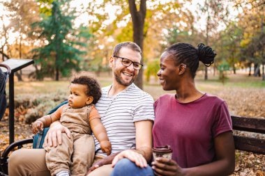 Karışık ırk çiftleri parktaki bir bankta oğullarıyla oturuyor..