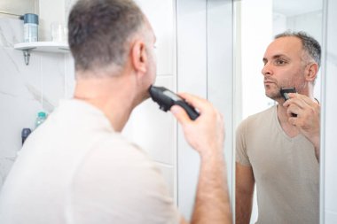 Adam banyoda tıraş makinesiyle sakalını kesiyor..