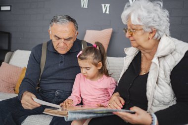 A child enjoys a storybook with her grandparents at home. clipart