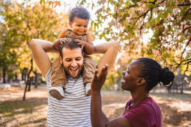 Boy in the arms of his parents in the park. clipart