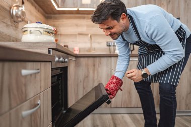 Kahverengi saçlı adam fırının kapısını açmak ve hazırladığı yemekleri kontrol etmek için uzandı..