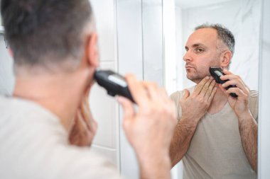 Adam banyoda tıraş makinesiyle sakalını kesiyor..