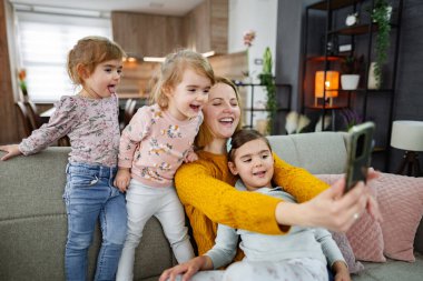 Anne ve üç kızı kanepede oturup evdeki oturma odasında selfie çekiyorlar..