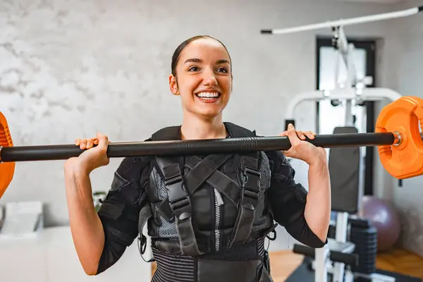 stock image A woman joyfully lifts weights while wearing EMS training gear.