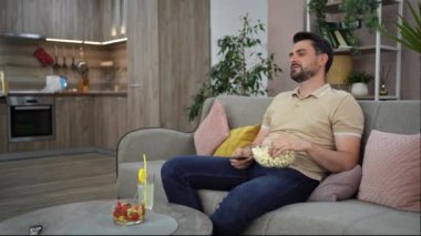 Sıcak bir oturma odasında gevşeyen bir adam, atıştırmalıkların ve içkilerin tadını çıkarıyor..