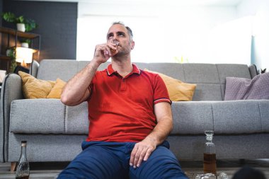 Olgun bir adam yerde oturup içki içiyor..