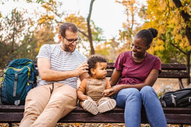 Karışık ırk çiftleri parktaki bir bankta oğullarıyla oturuyor..