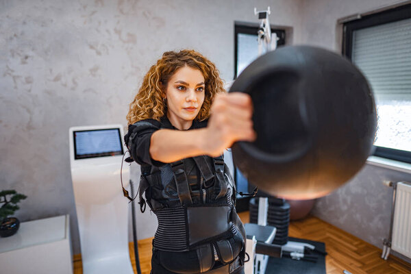 A woman focuses on lifting a kettlebell while using body-enhancing gear.