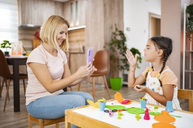 Bir anne kızının resmini çeker ve rahat oturma odalarında renkli mankenlerle resim yaparken eğlenir..