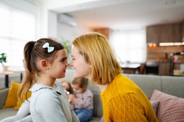 Anne en büyük kızıyla yakın temasta iken diğer iki kız kardeş oturma odasının arka planında koltukta oturuyor..