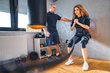 A coach supports a woman using resistance training equipment in a gym. clipart