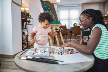 A joyful mother and child share a painting activity at home. clipart