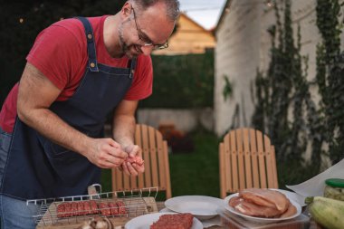 Neşeli bir aşçı arka bahçedeki barbekü etkinliğini düzenlerken eti süslüyor.