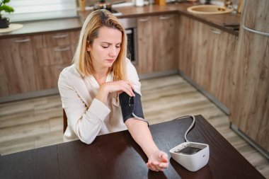 Genç bir kadın mutfak ortamında kan basıncını ölçer..