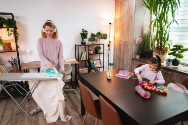 Bir anne, çocuğu yemek masasında oynarken kıyafetlerini ütüler..