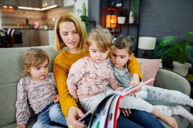 Anne ve üç kızı oturma odasında kanepede oturmuş annelerinin bir hikaye okumasını dikkatle dinliyorlar..