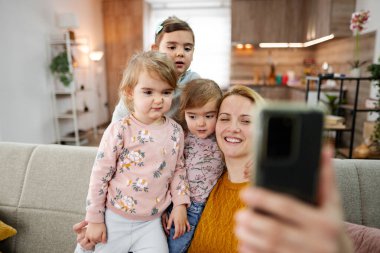 Anne ve üç kızı kanepede oturup evdeki oturma odasında selfie çekiyorlar..