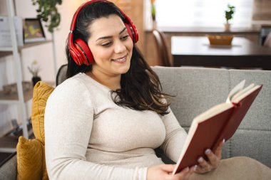 Kablosuz kulaklıklı kadın kanepede kitap okuyor..